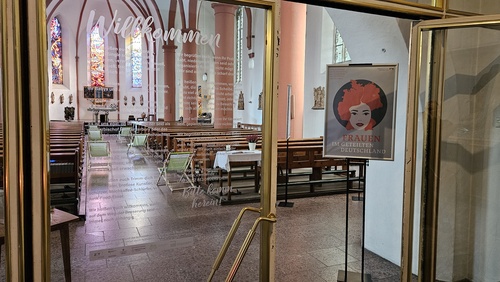 Blick in einen Kirchenraum, in dem ein Plakat auf die Ausstellung hinweist