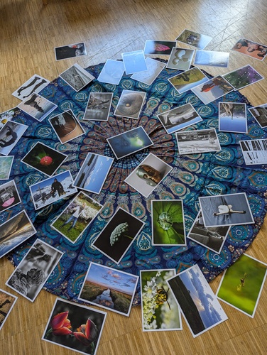 Unterschiedliche Fotopostkarten lieben ausgebreitet auf einem runden, blau-gemusterten Tuch auf einem Holfzfußboden.