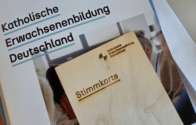 Veranstaltungsunterlagen der Katholischen Erwachsenenbildung in Deutschland: Eine Mappe mit Schriftzug und eine Stimmkarte aus Holz.