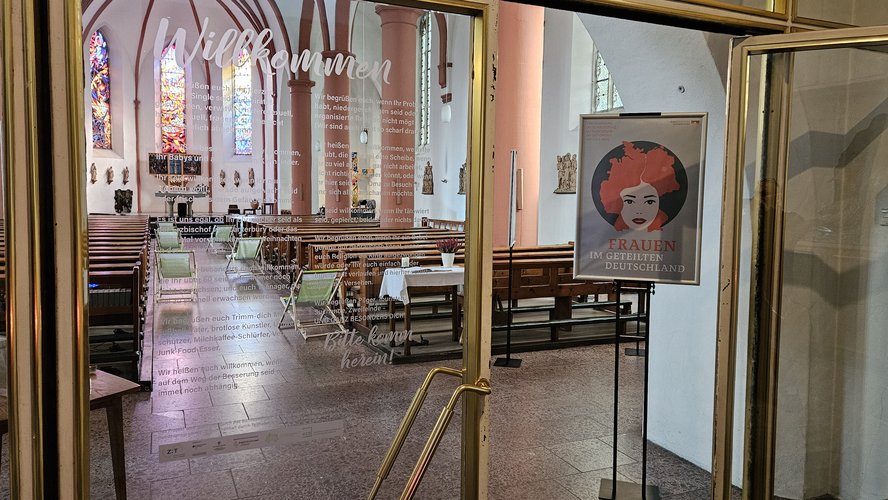 Blick in einen Kirchenraum, in dem ein Plakat auf die Ausstellung hinweist